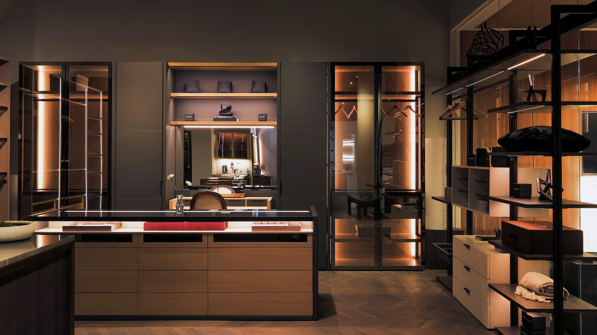 Luxury walk-in closet with integrated vanity, illuminated glass doors, and a wood island dresser. Luxury walk-in closet with integrated vanity, illuminated glass doors, and a wood island dresser.