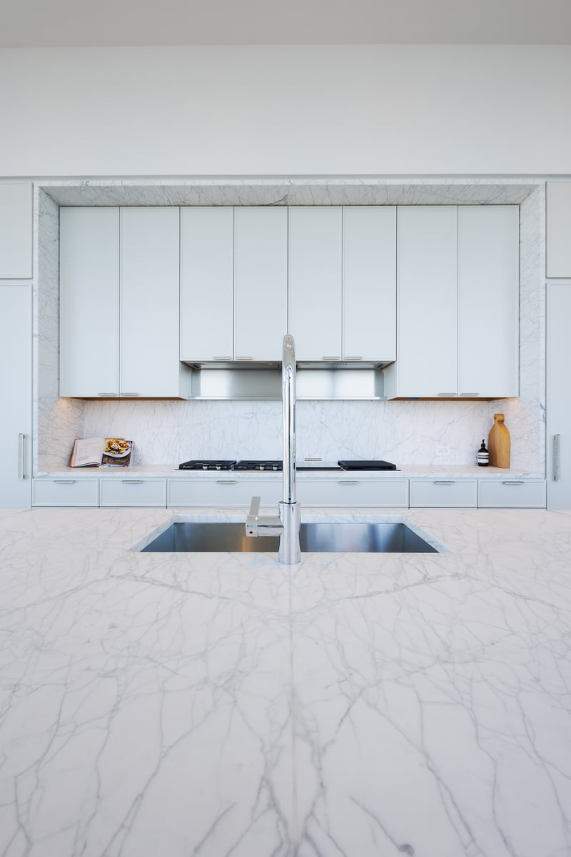 Minimalist kitchen with marble waterfall island, matching marble backsplash, and sleek white cabinetry. Minimalist kitchen with marble waterfall island, matching marble backsplash, and sleek white cabinetry.